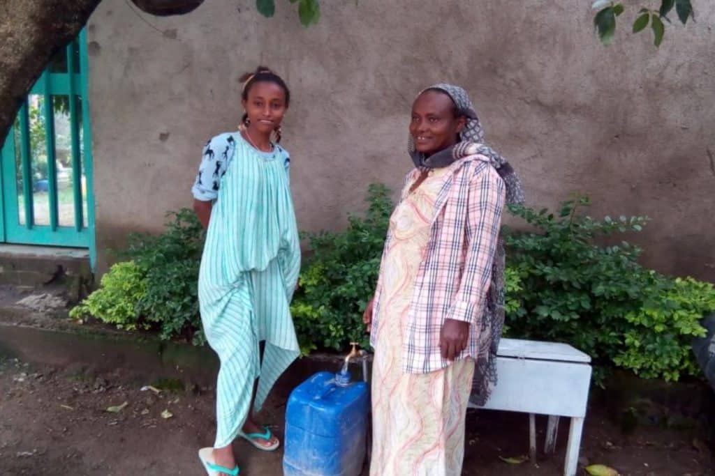 Gadisa Hurisa met haar dochter Bilusema Getachew tappen water uit de kraan bij hun huis in Adama, DebeSoloke kebele, Soloko Kurfa village. Juli 2020.