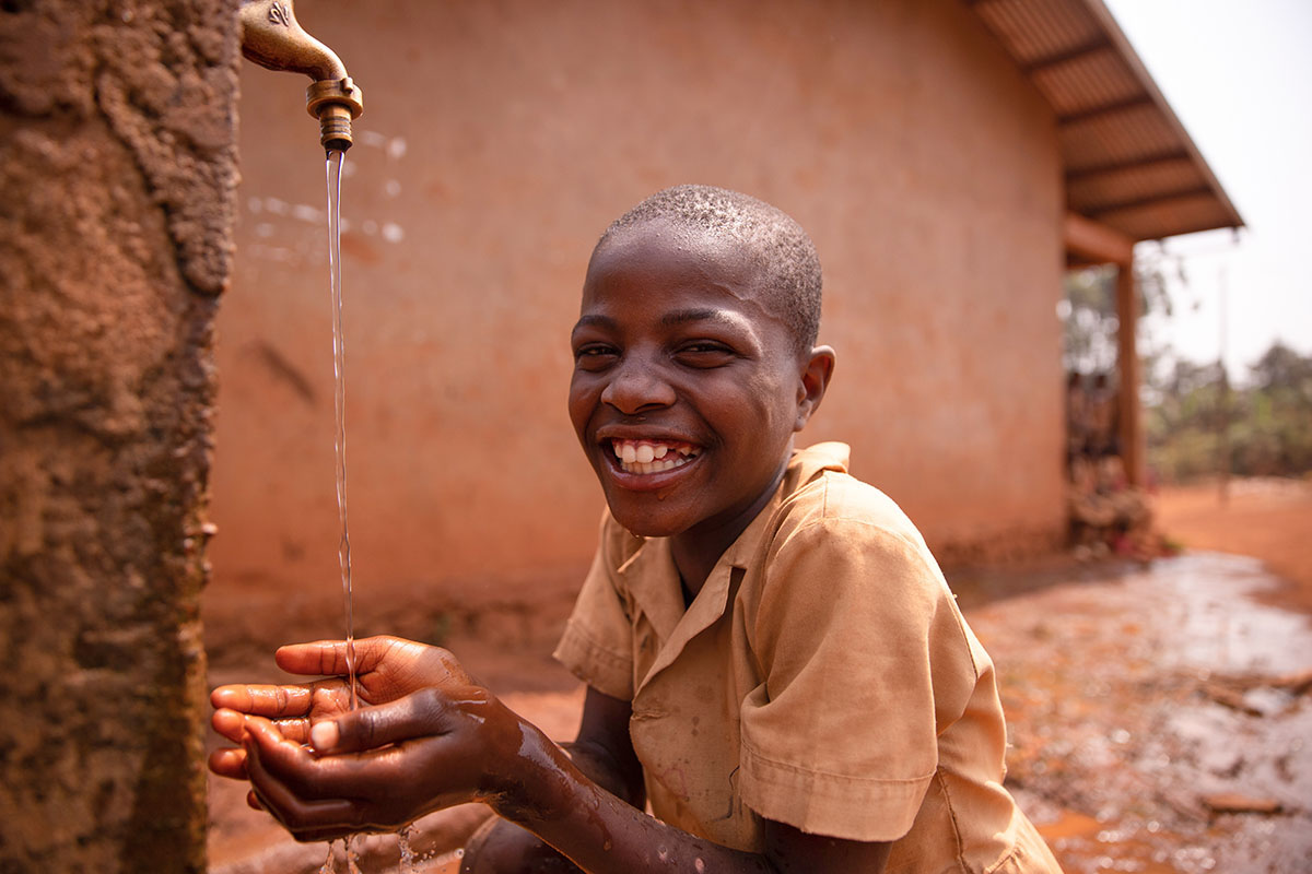 Smiling black african schoolboy drinking from a tap outside