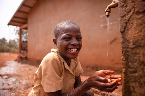 Smiling african school boy drinking from a tap outside