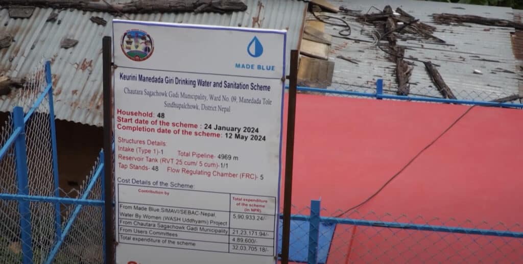 Government signage at water point in Nepal showing data like number of households connected and Made Blue logo